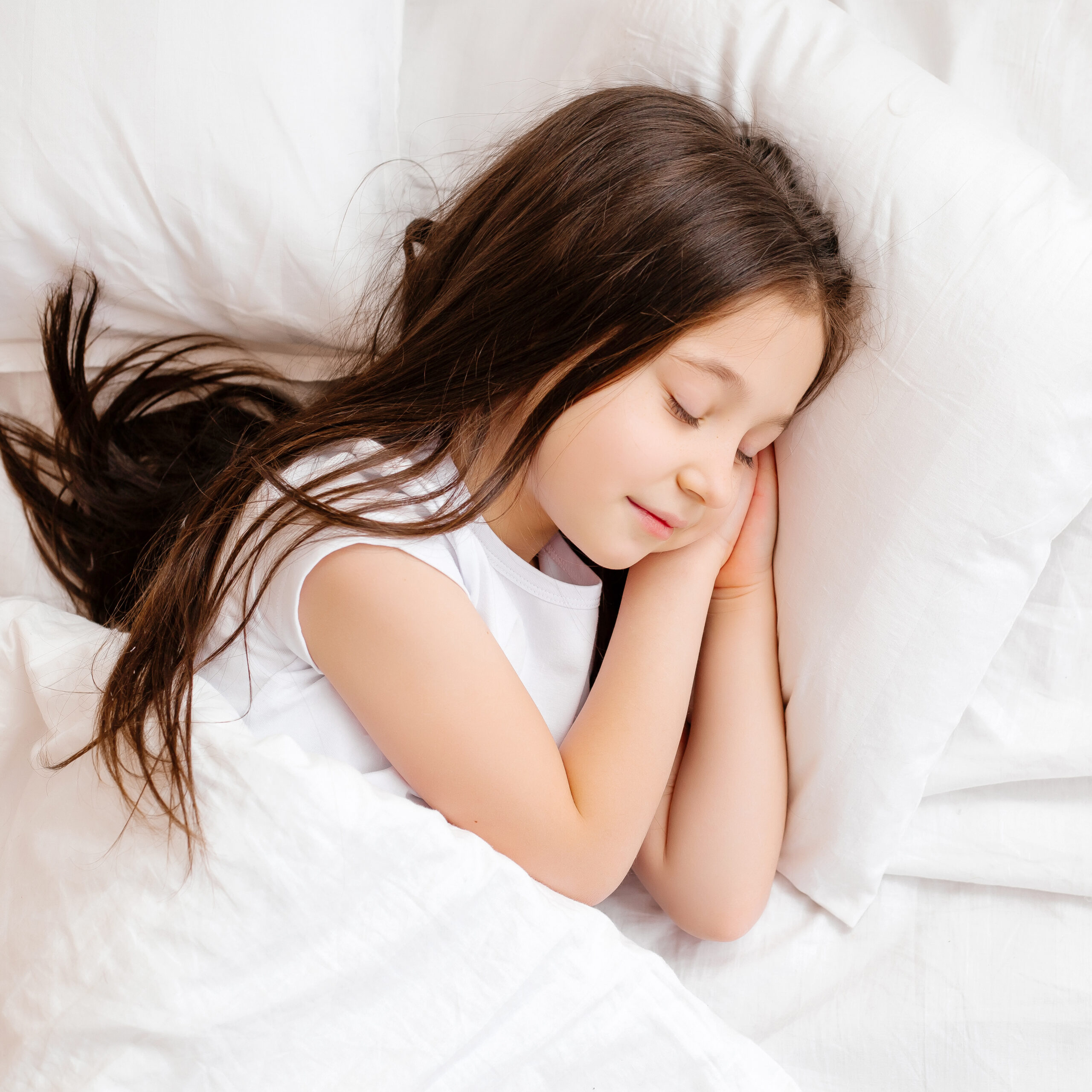 Little brunette girl sleeps sweetly in bed with white linen. space for text. healthy baby's sleep